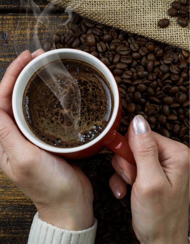 Weibliche Hände mit einer Kaffeetasse und frischem Kaffee in der Hand